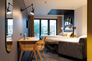 Habitación de hotel con cama, escritorio, silla, sofá y un amplio ventanal con vistas.