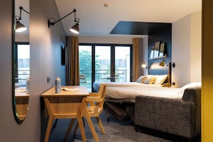 Habitación de hotel con cama, escritorio, silla, sofá y un amplio ventanal con vistas.
