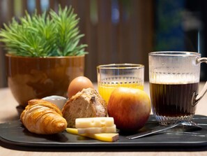 Bandeja de desayuno con croissant, queso, manzana, pan y una taza de café.