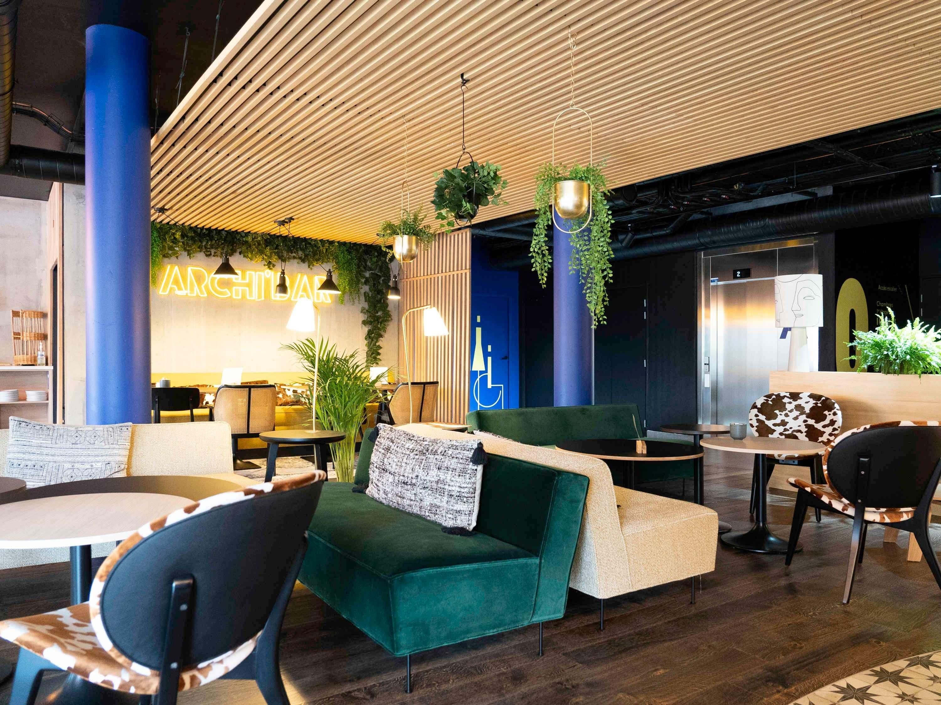 A modern lounge area with seating, hanging plants, and a neon sign.