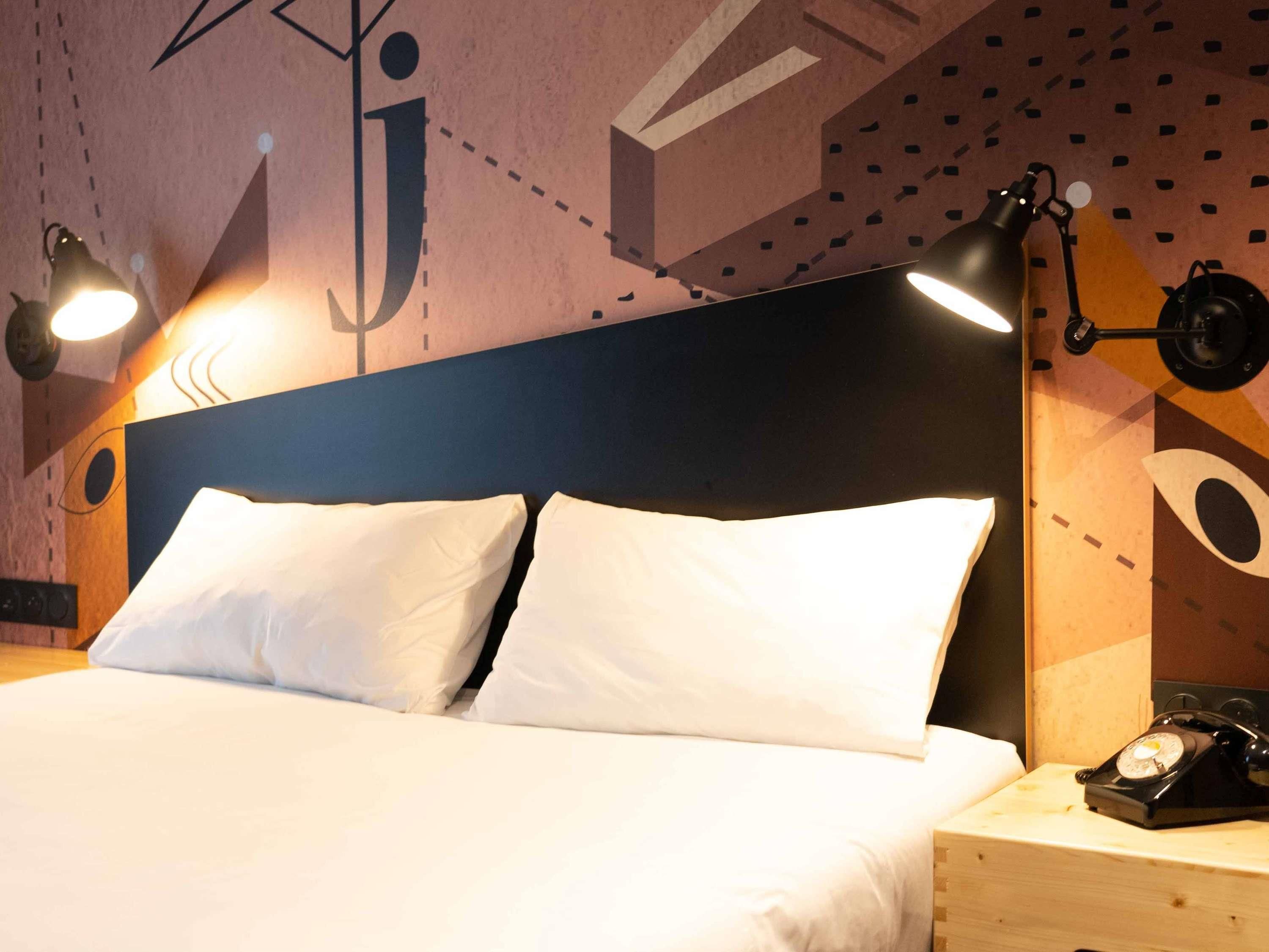 Ein Bett mit weißer Bettwäsche, einem hölzernen Kopfteil und einem Nachttisch mit Wählscheibentelefon.