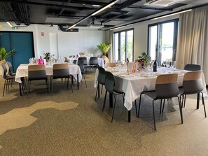 Comedor con mesas dispuestas para una comida, sillas y plantas en macetas.