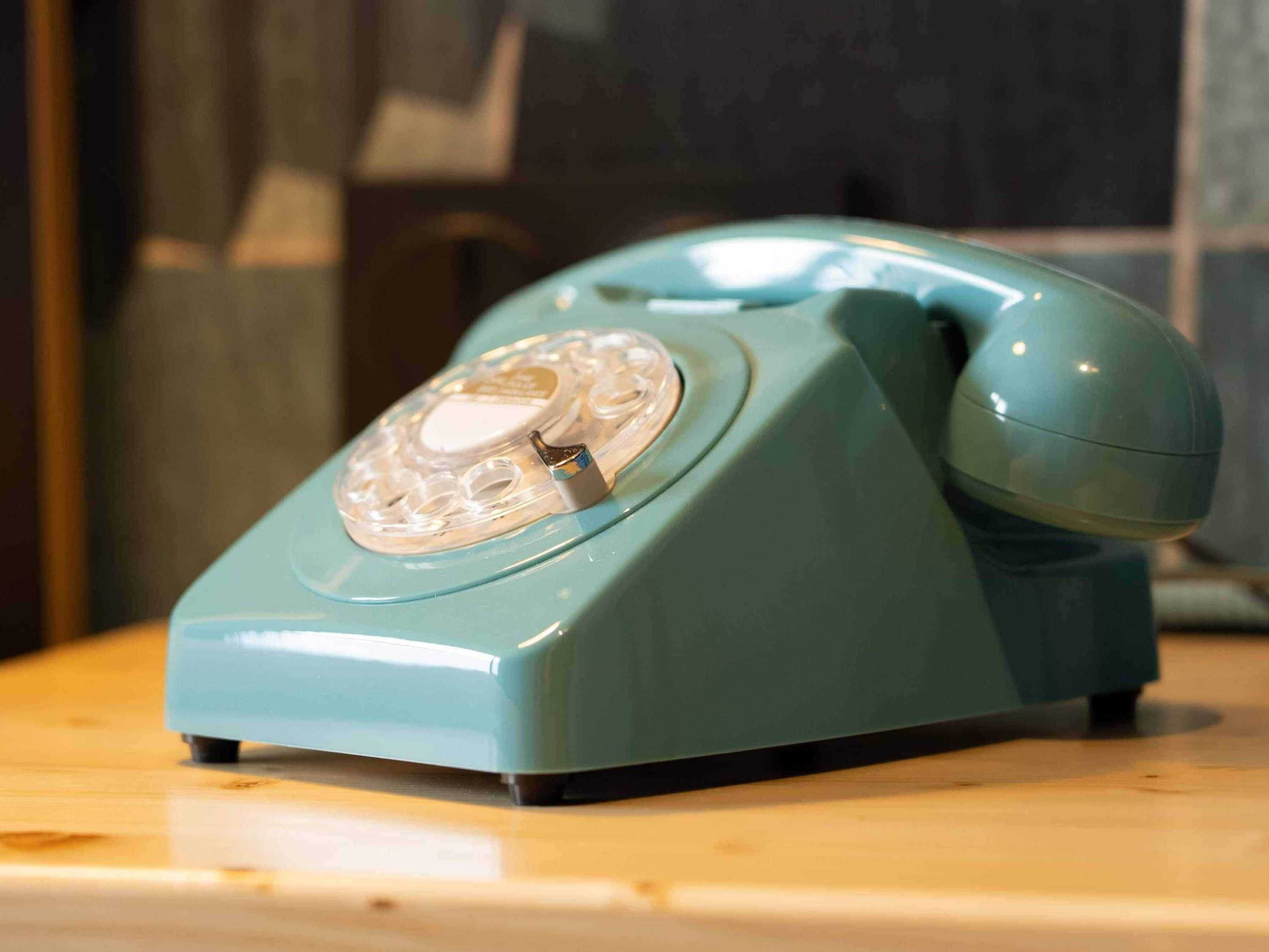A teal rotary telephone on a wooden surface.