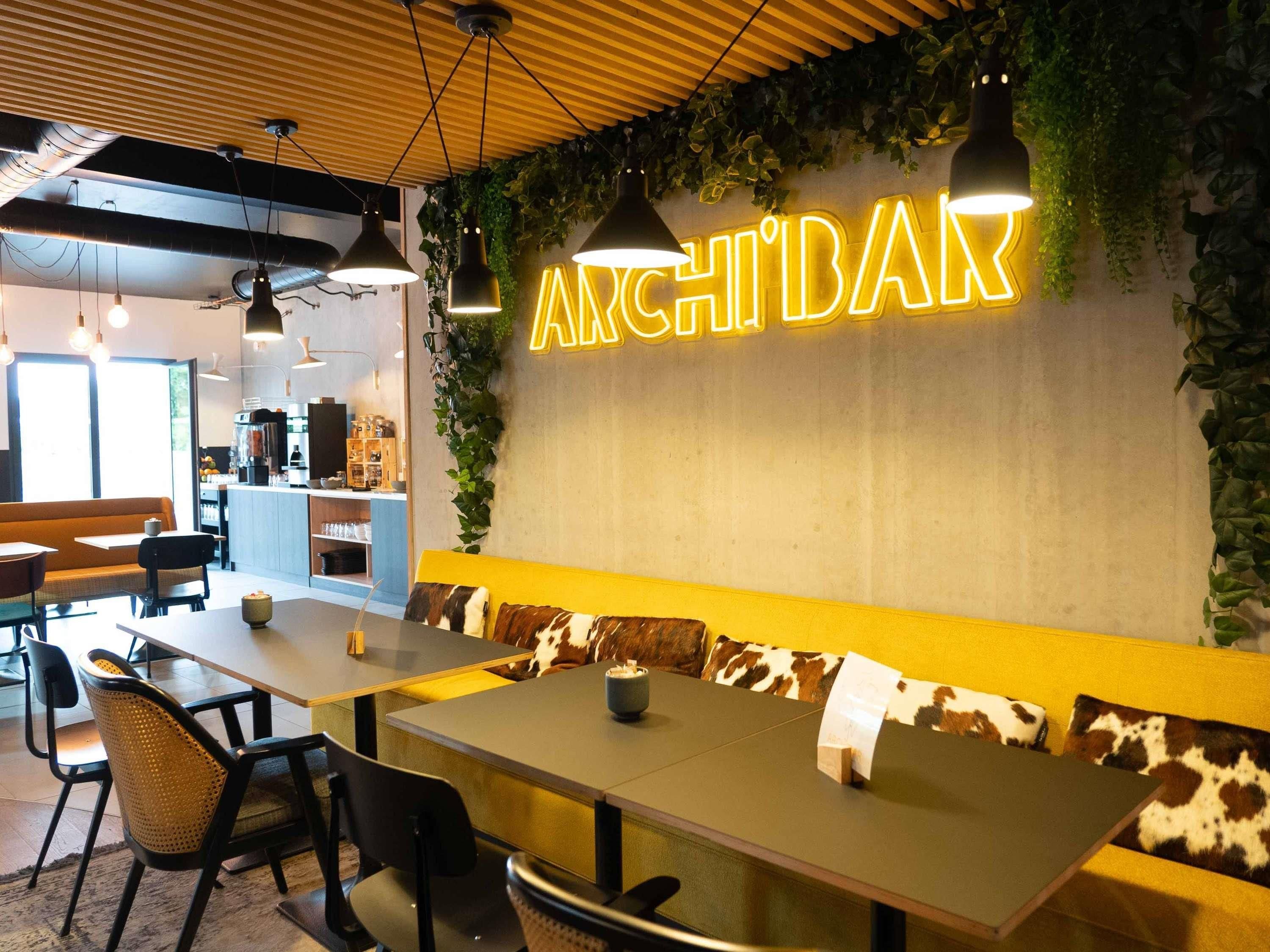 Un interior moderno con un letrero de neón que dice 'ARCHIDAR', techo de madera y una zona de estar con un banco y sillas.