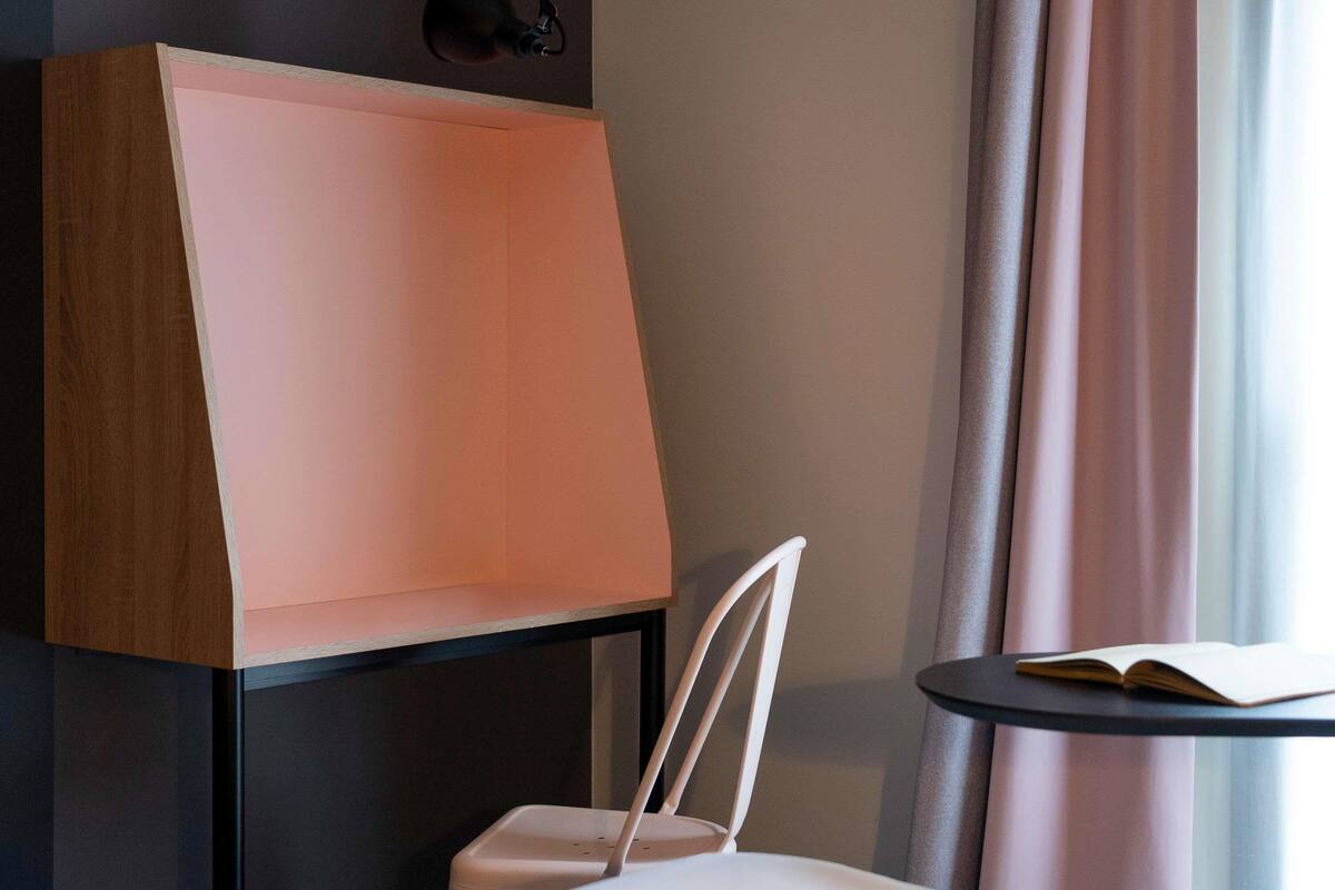 Una habitación con una silla blanca, una mesa, una lámpara y un ventanal con cortinas.