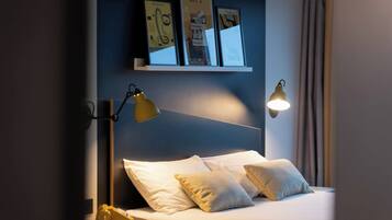 Habitación de hotel con una cama, dos lámparas de noche, un teléfono y una estantería con fotografías enmarcadas.