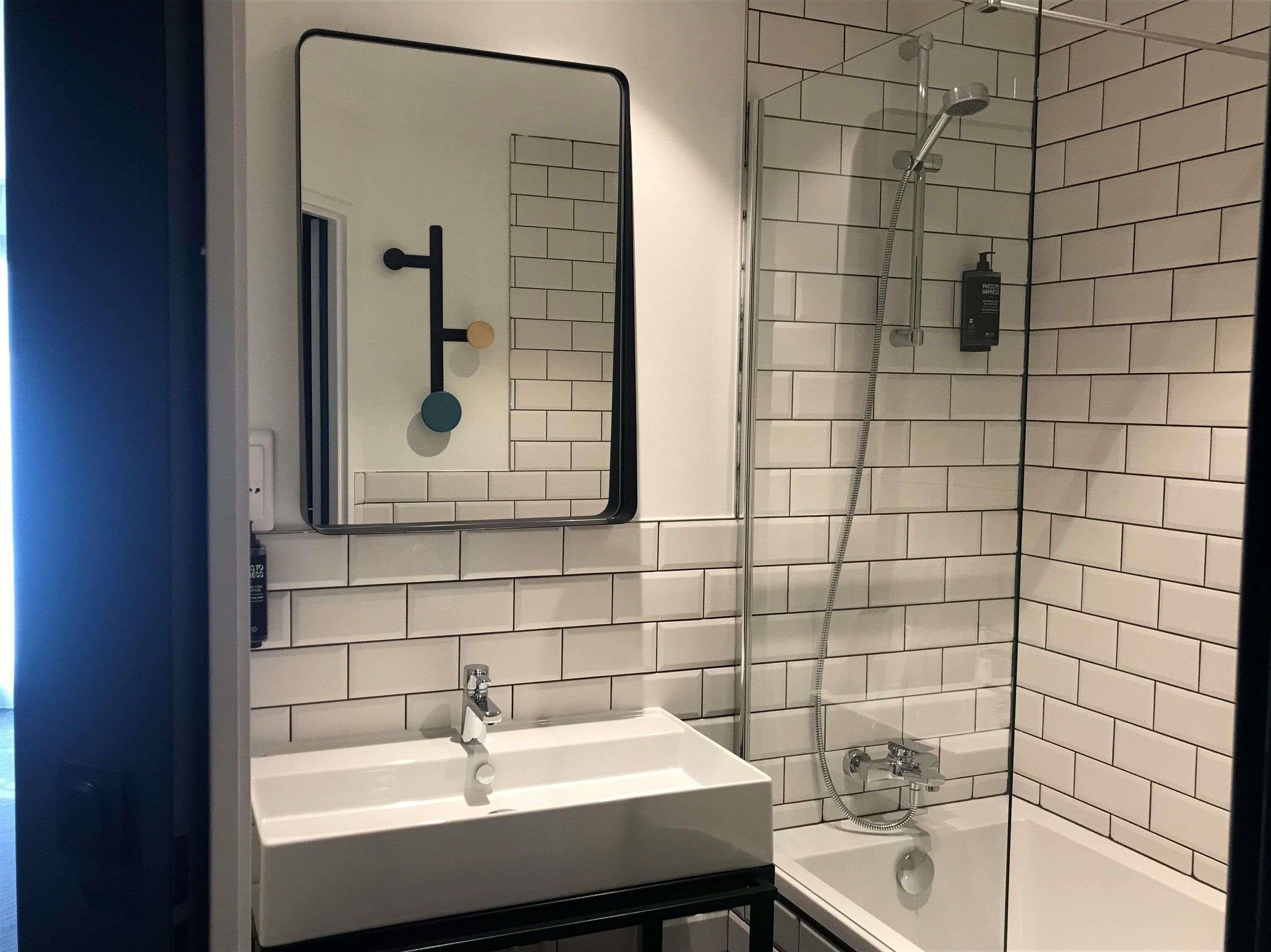 A bathroom with a white sink, a mirror, a shower with a glass door, and a tiled wall.