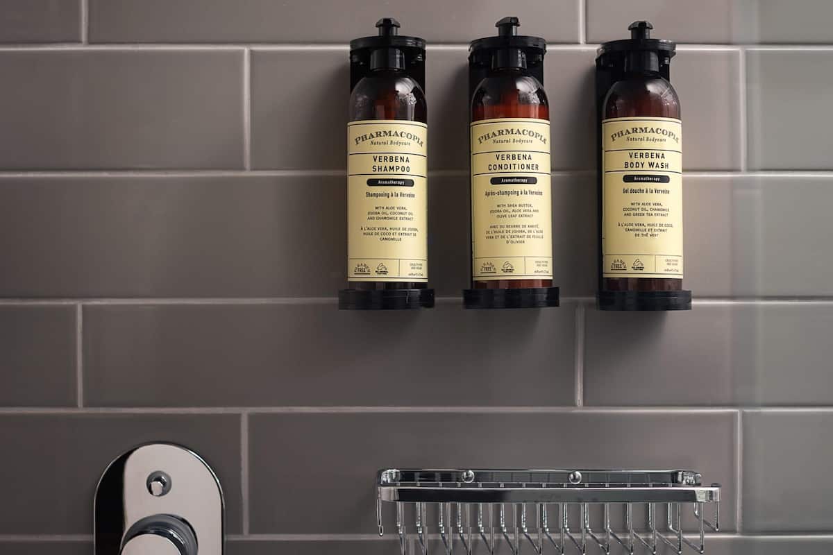 Tres botellas de jabón de baño y champú de verbena sobre una pared de azulejos.