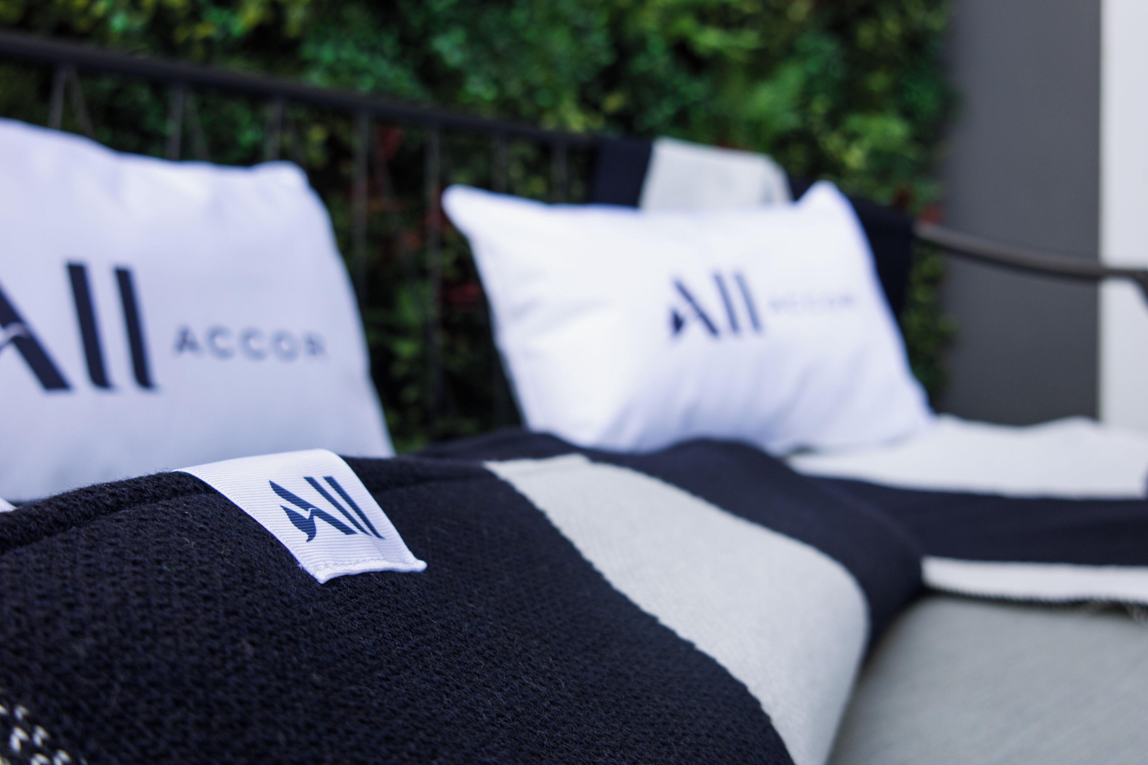A bed with pillows and a blanket, with a blurred background of greenery.