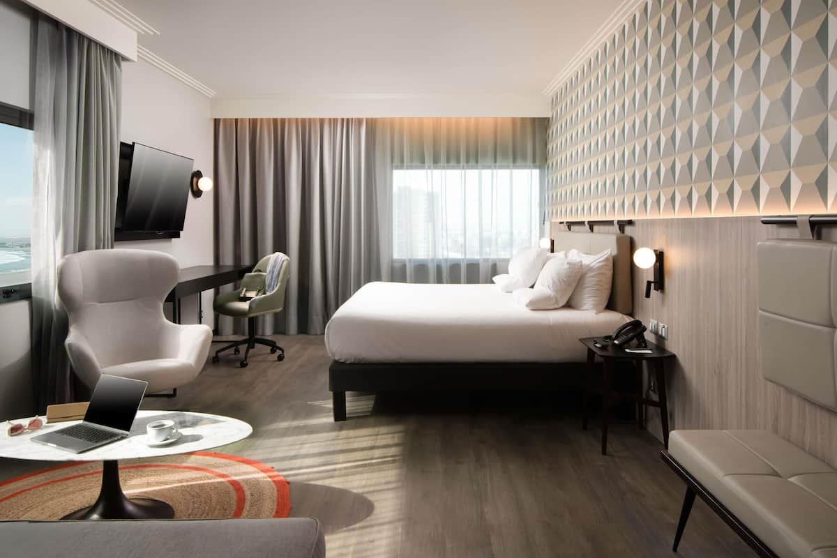Ein Hotelzimmer mit Bett, Schreibtisch mit Laptop, Stuhl, Fernseher und Blick auf die Stadt.