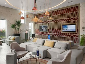 A modern living room with a sectional sofa, a coffee table, a laptop, and a television mounted on a red and white patterned wall. - Novotel Arica (Arica)