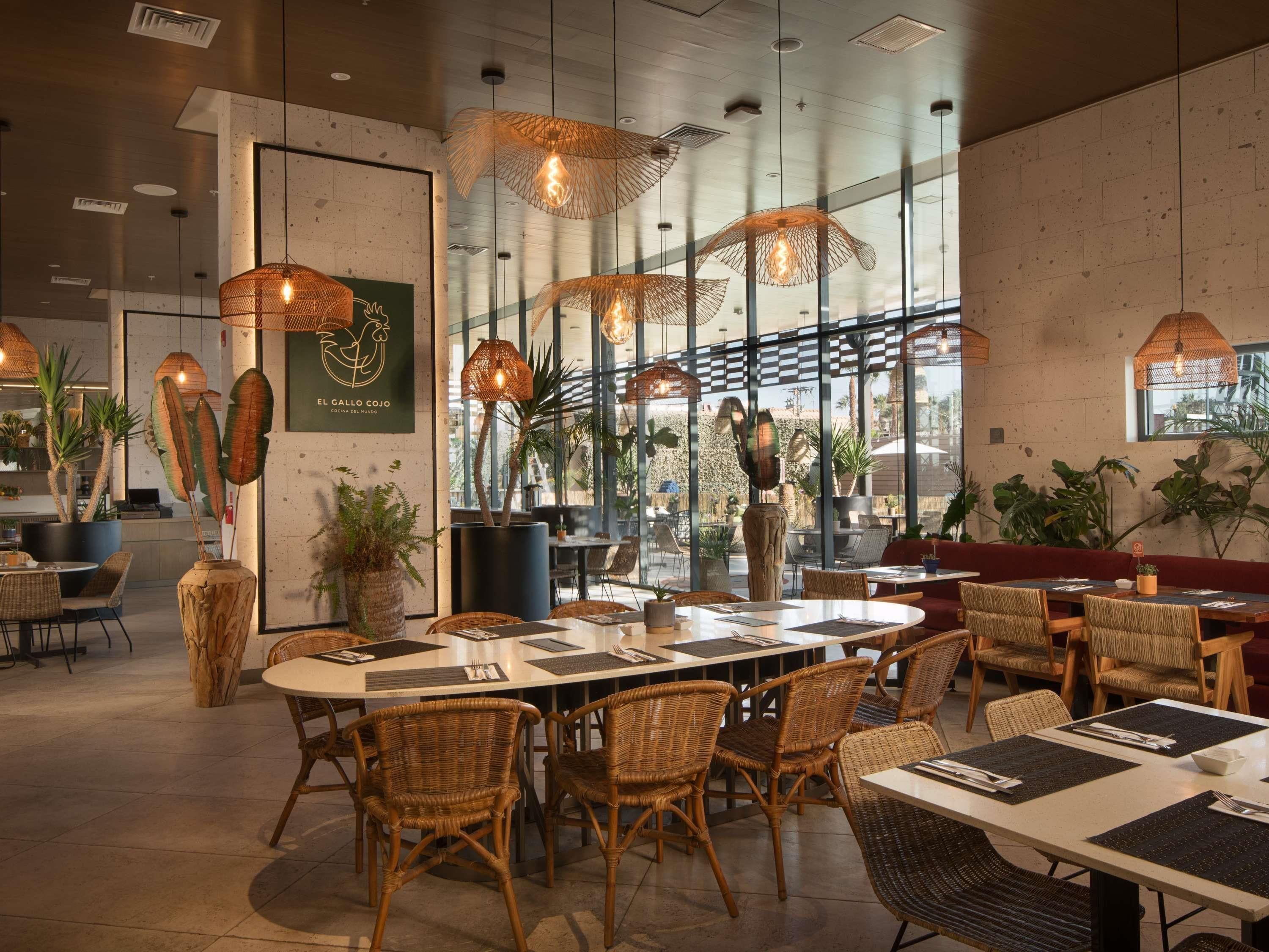 Een restaurantinterieur met rieten meubels, hanglampen en grote ramen.