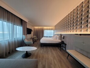 A modern hotel room with a bed, two armchairs, a small round table, a bench, and a geometric-patterned wall. - Novotel Arica (Arica)