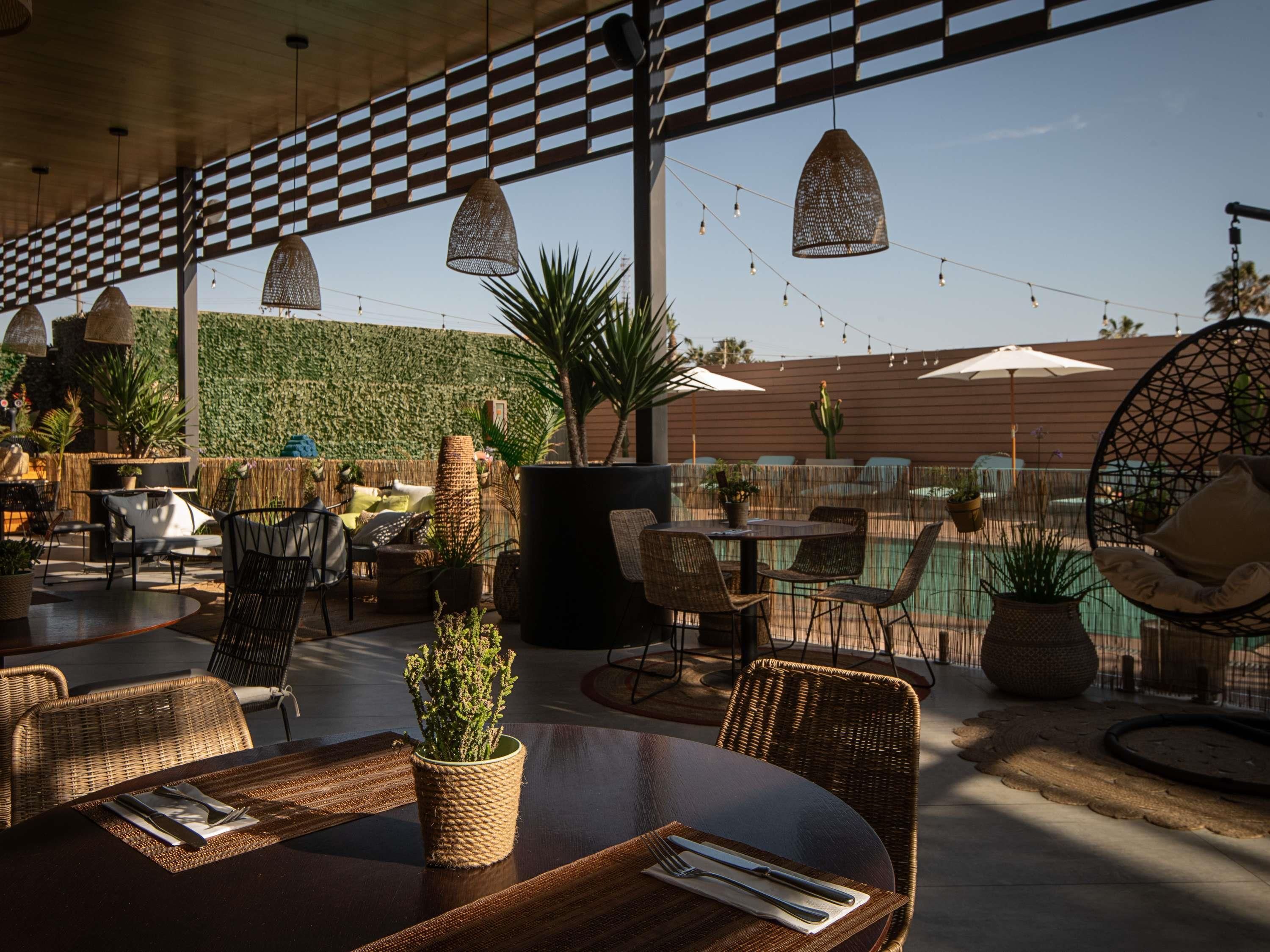An outdoor dining area with wicker furniture, string lights, and a view of a pool.