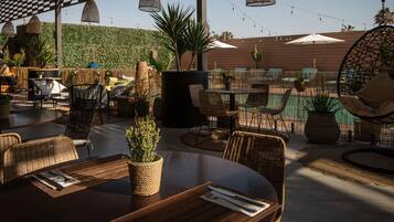 An outdoor dining area with wicker furniture, string lights, and a view of a pool.
