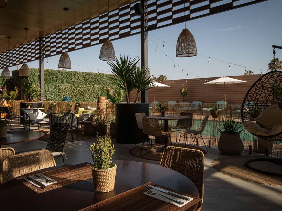 An outdoor dining area with wicker furniture, string lights, and a view of a pool.