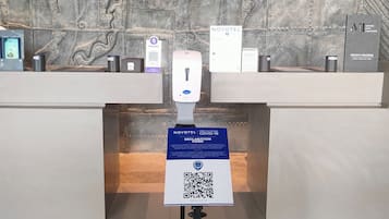 A hotel reception desk with a QR code for COVID-19 declaration, a phone card dispenser, and a Novotel sign.