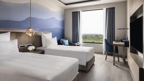 Ein Hotelzimmer mit zwei Betten, einem Schreibtisch, einem Stuhl, einem Fernseher und einem großen Fenster mit Blick.