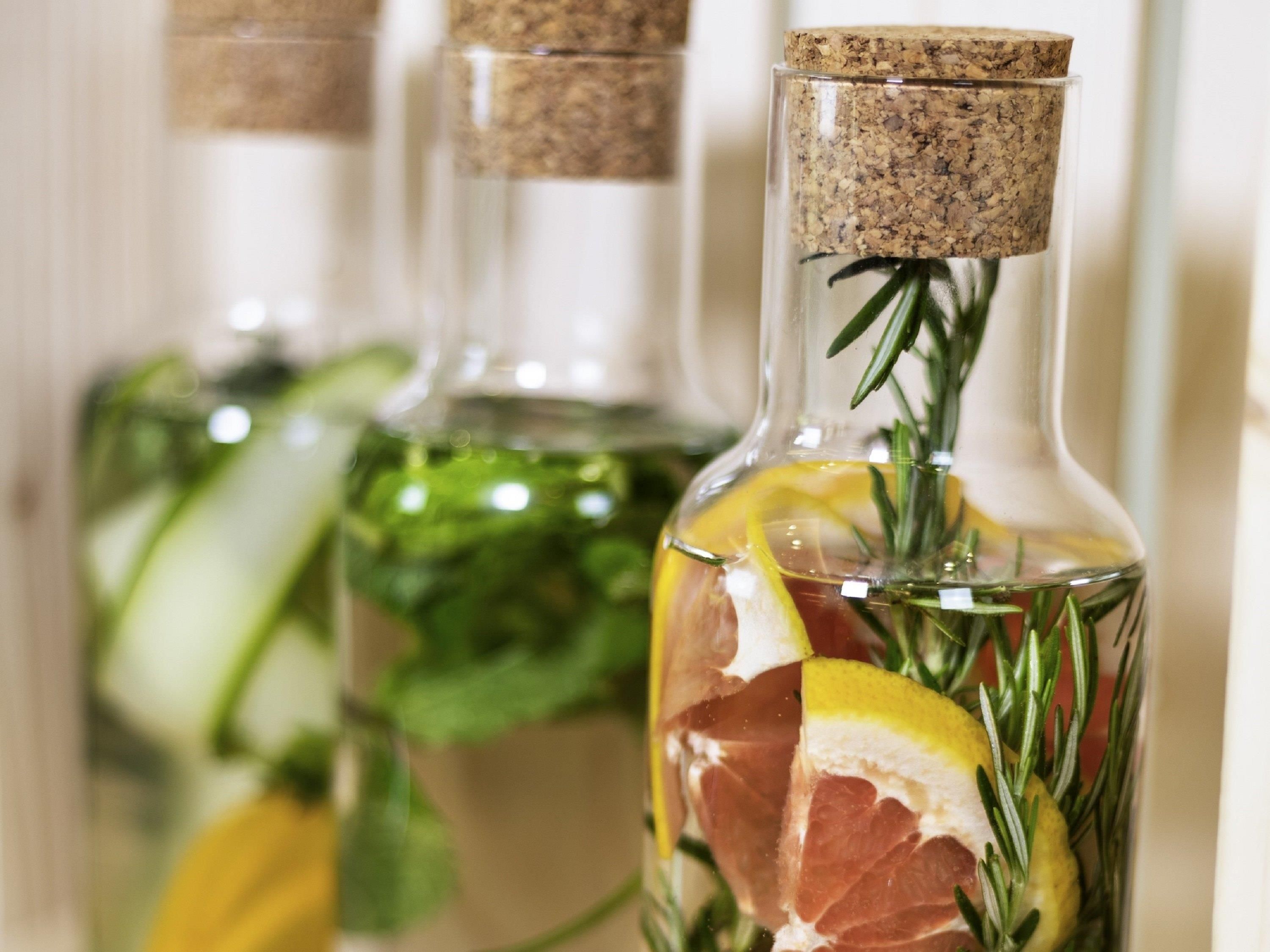 Tres botellas de vidrio con tapones de corcho, llenas de agua, con rodajas de limón, romero y un trozo de carne.