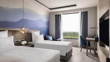 Habitación de hotel con dos camas, un escritorio, una silla, un televisor y un ventanal con vistas.