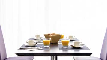 A dining table with breakfast items, two cups, and a basket of bread.
