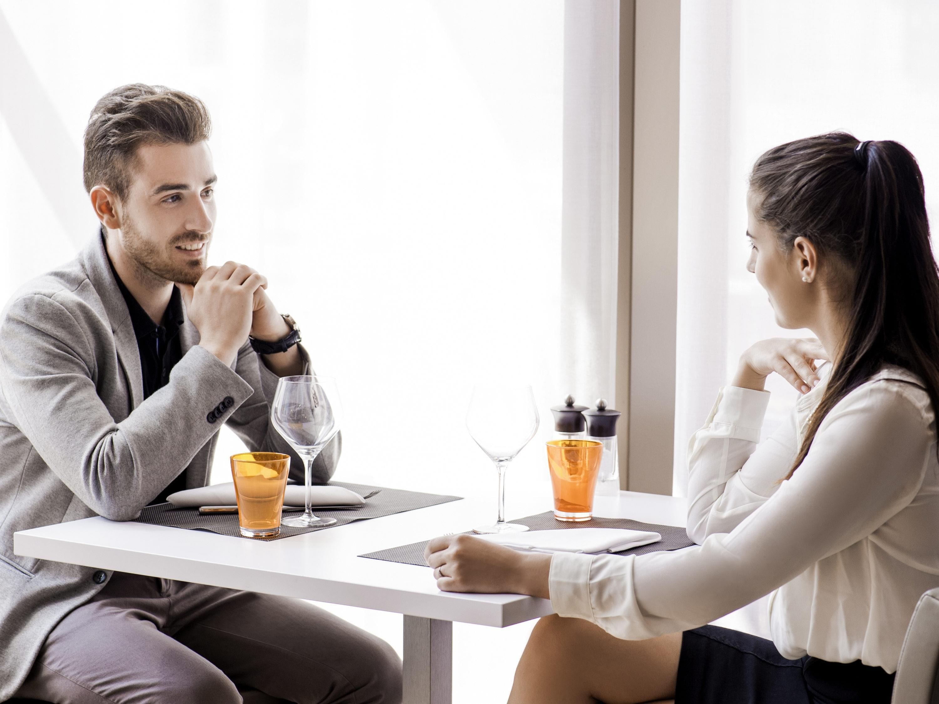 A man and a woman sitting at a table with drinks and a notebook.