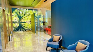 Eine moderne Lobby mit einer großen Baum-Mural, zwei blauen Sesseln mit Kissen und einem glänzenden Marmorboden.