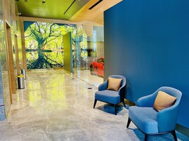 Un vestíbulo moderno con un gran mural de árboles, dos sillones azules con cojines y un piso de mármol brillante.