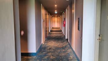 Pasillo de hotel con alfombra estampada, puertas a ambos lados y un extintor de incendios en la pared.
