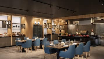 Una cocina moderna con electrodomésticos integrados, armarios de madera y una zona de comedor con sillas azules y una mesa de mármol.