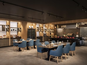 Una cocina moderna con electrodomésticos integrados, armarios de madera y una zona de comedor con sillas azules y una mesa de mármol.