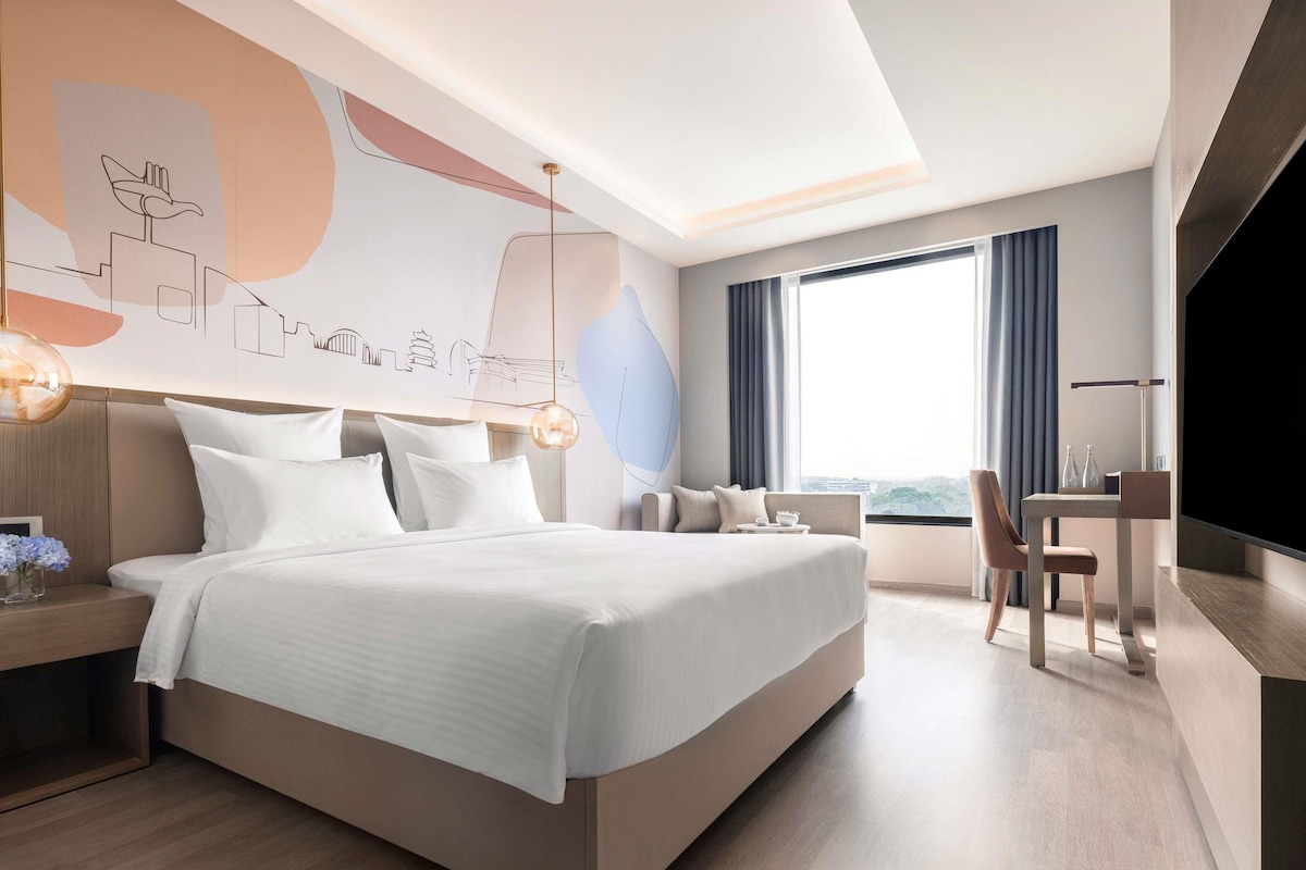 Ein modernes Hotelzimmer mit einem großen Bett, einem Schreibtisch, einem Sessel und einem Fernseher.