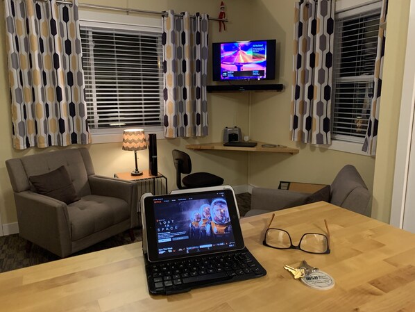 A cozy living room with a sofa, a coffee table with a laptop, a TV, and patterned curtains.