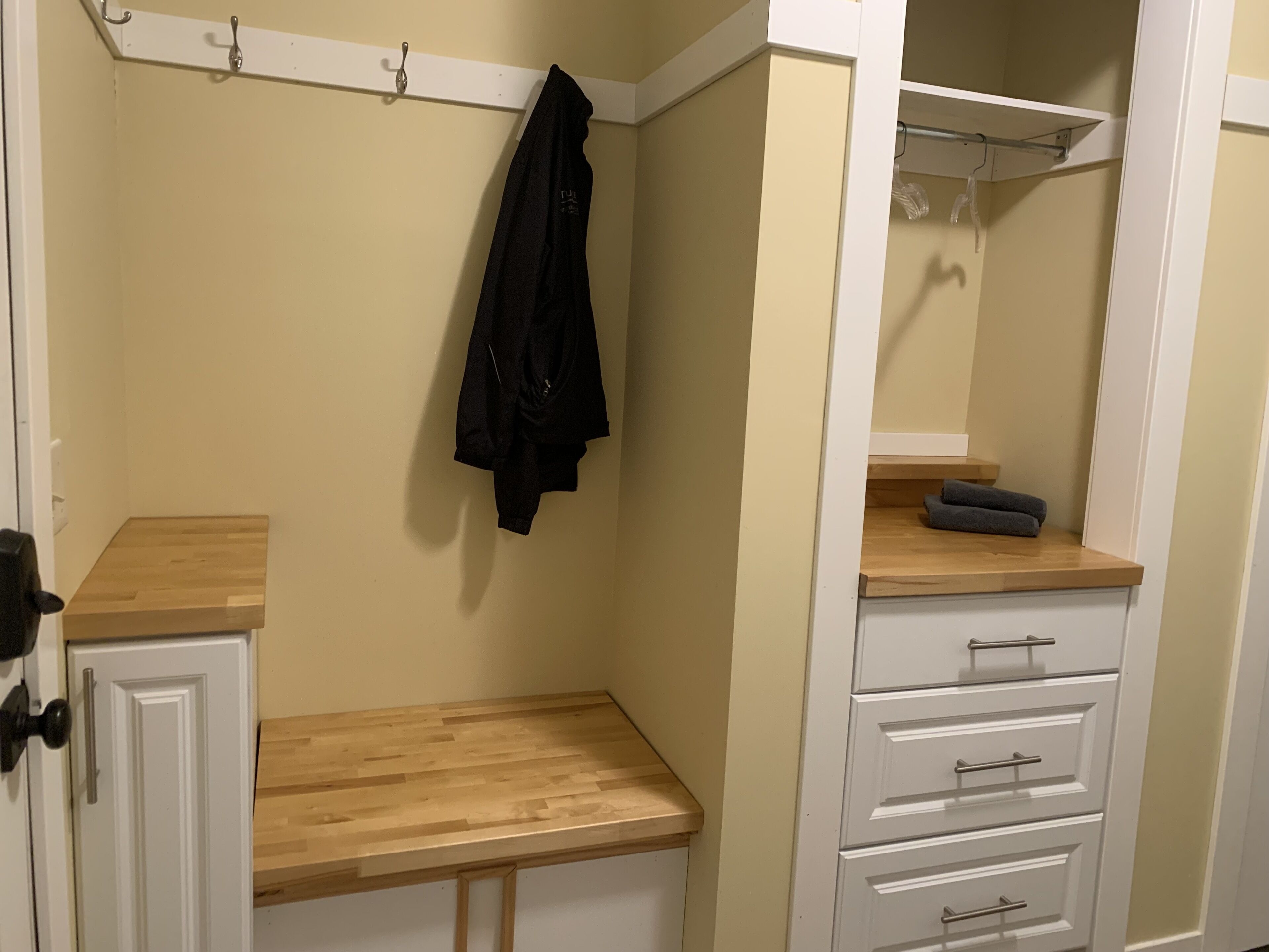 A room with a wooden bench, a white cabinet with drawers, a coat rack, and a mirror.