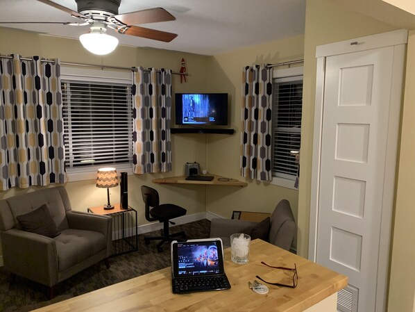 Un salon avec un canapé, une table basse sur laquelle se trouve un ordinateur portable, un téléviseur et un ventilateur de plafond.