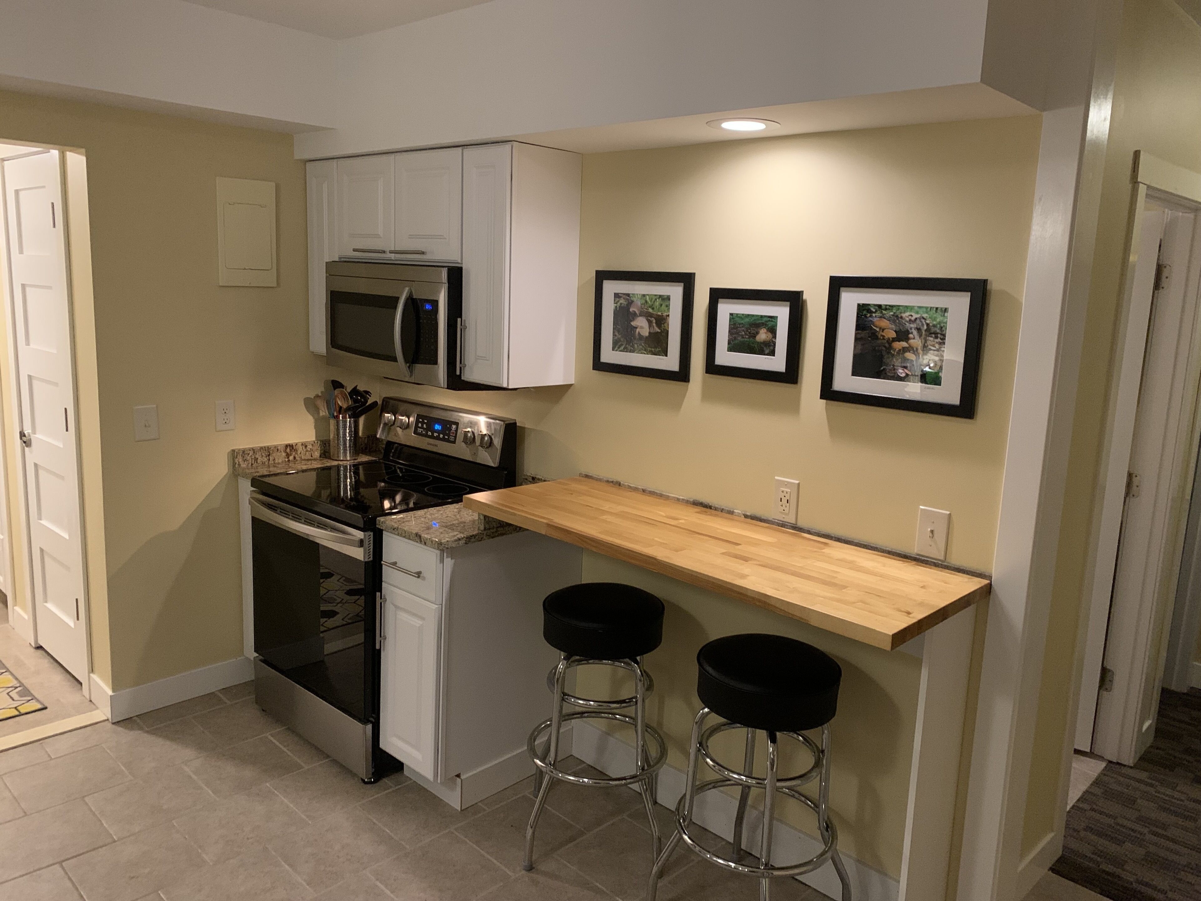 A compact kitchen with white cabinets, a microwave, a stove, and two bar stools.