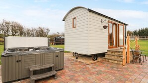 A hot tub and a small cabin with a wooden door and windows, both on a brick patio. - Highland View (Rhayader)