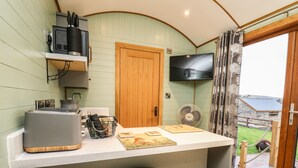 A kitchen with a wooden door, a TV mounted above it, and a small bar area with stools. - Highland View (Rhayader)