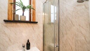 A bathroom with a marble sink, a glass shower enclosure, and a wooden shelf with decorative items. - Highland View (Rhayader)