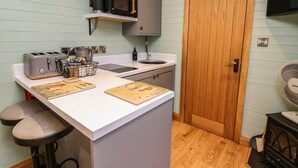 A compact kitchen with a microwave, toaster, sink, and wooden door. - Highland View (Rhayader)