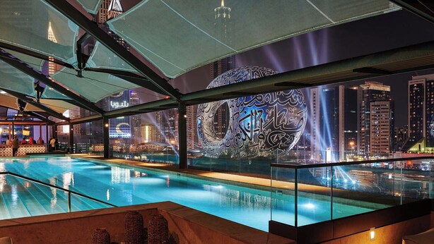 A modern indoor pool with a cityscape view, featuring a large illuminated artwork on the wall.