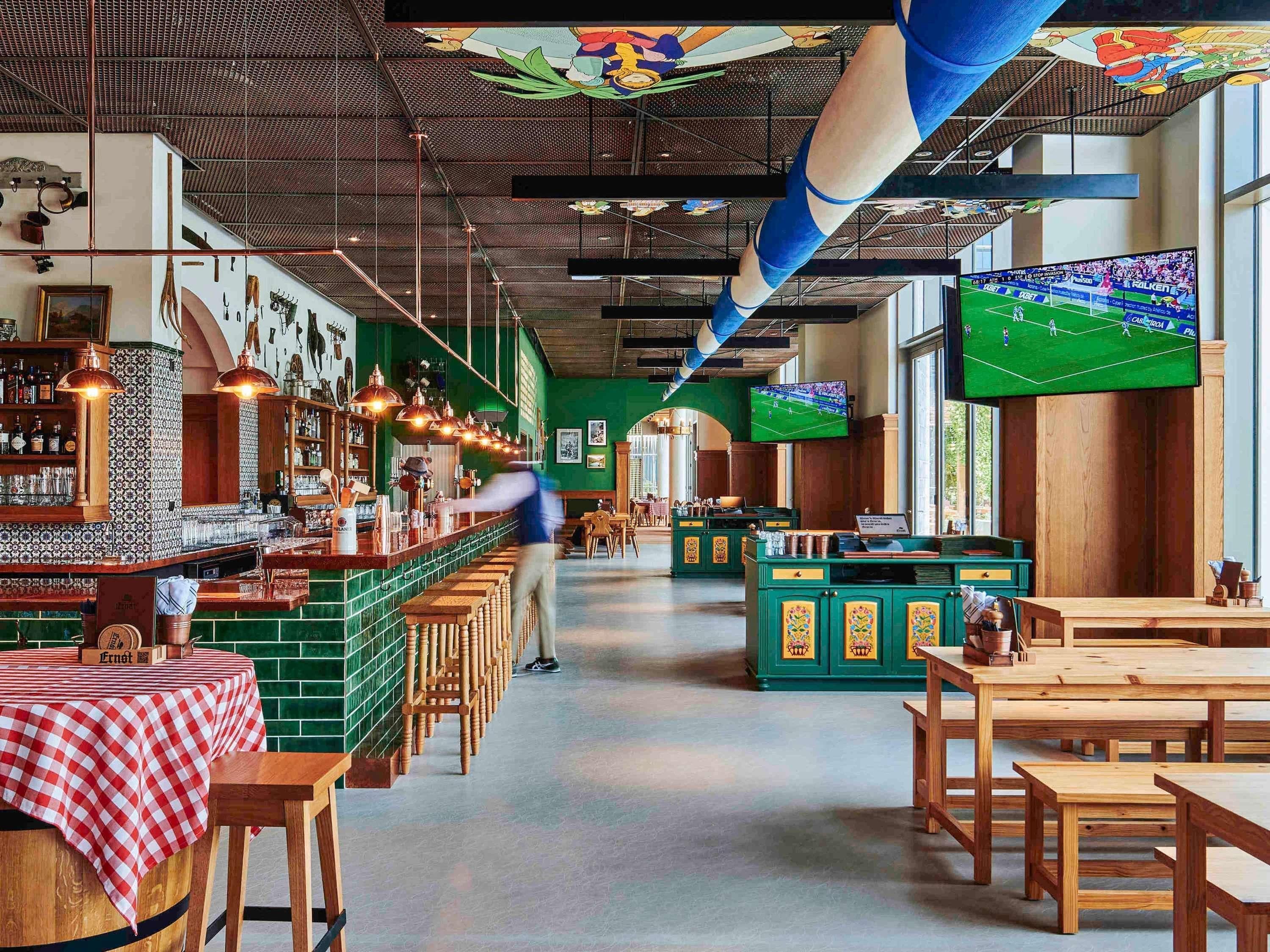 Een bar met een geruit tafelkleed, houten krukken en een bar met flessen en glazen.