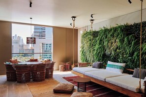 A modern living room with a city view, a hanging plant wall, and a cozy seating area. - 25hours Hotel Dubai One Central (Dubai)