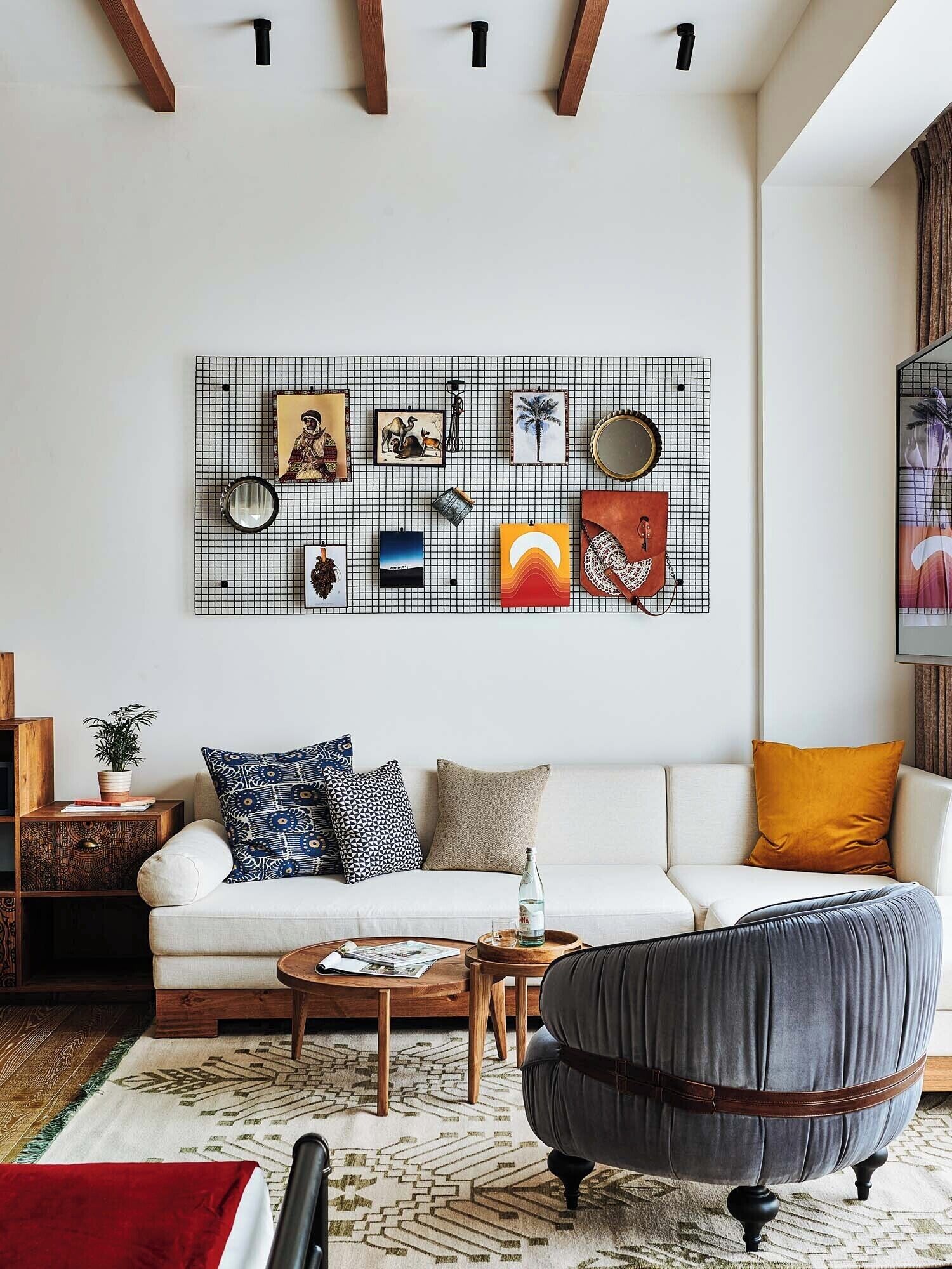 A modern living room with a white sofa, patterned cushions, a grey armchair, and a coffee table. A grid wall art piece hangs above the sofa.