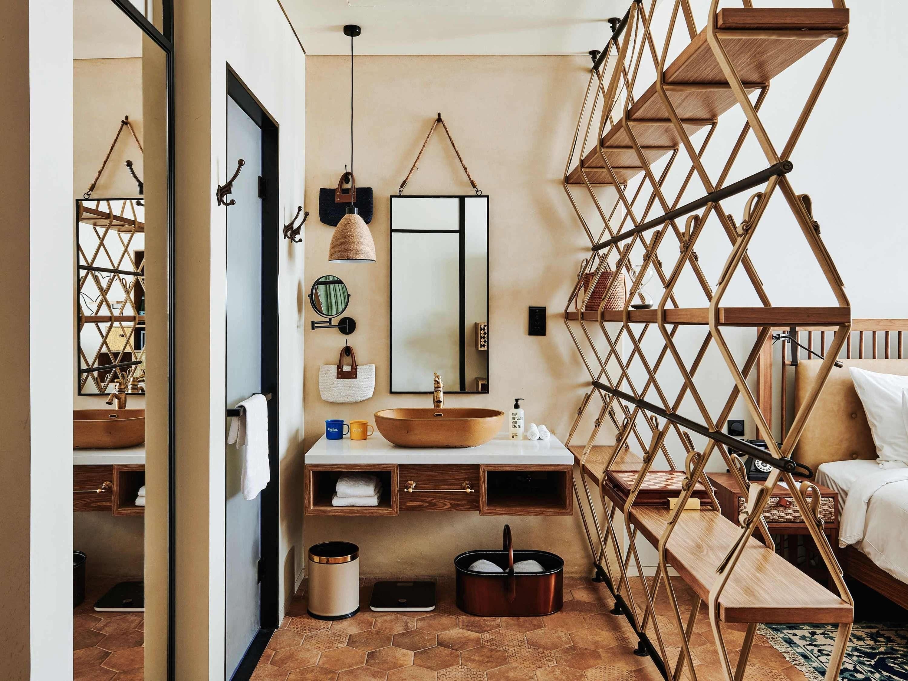 A compact hotel bathroom with a wooden vanity, a large mirror, a hanging light fixture, and a built-in shelf.