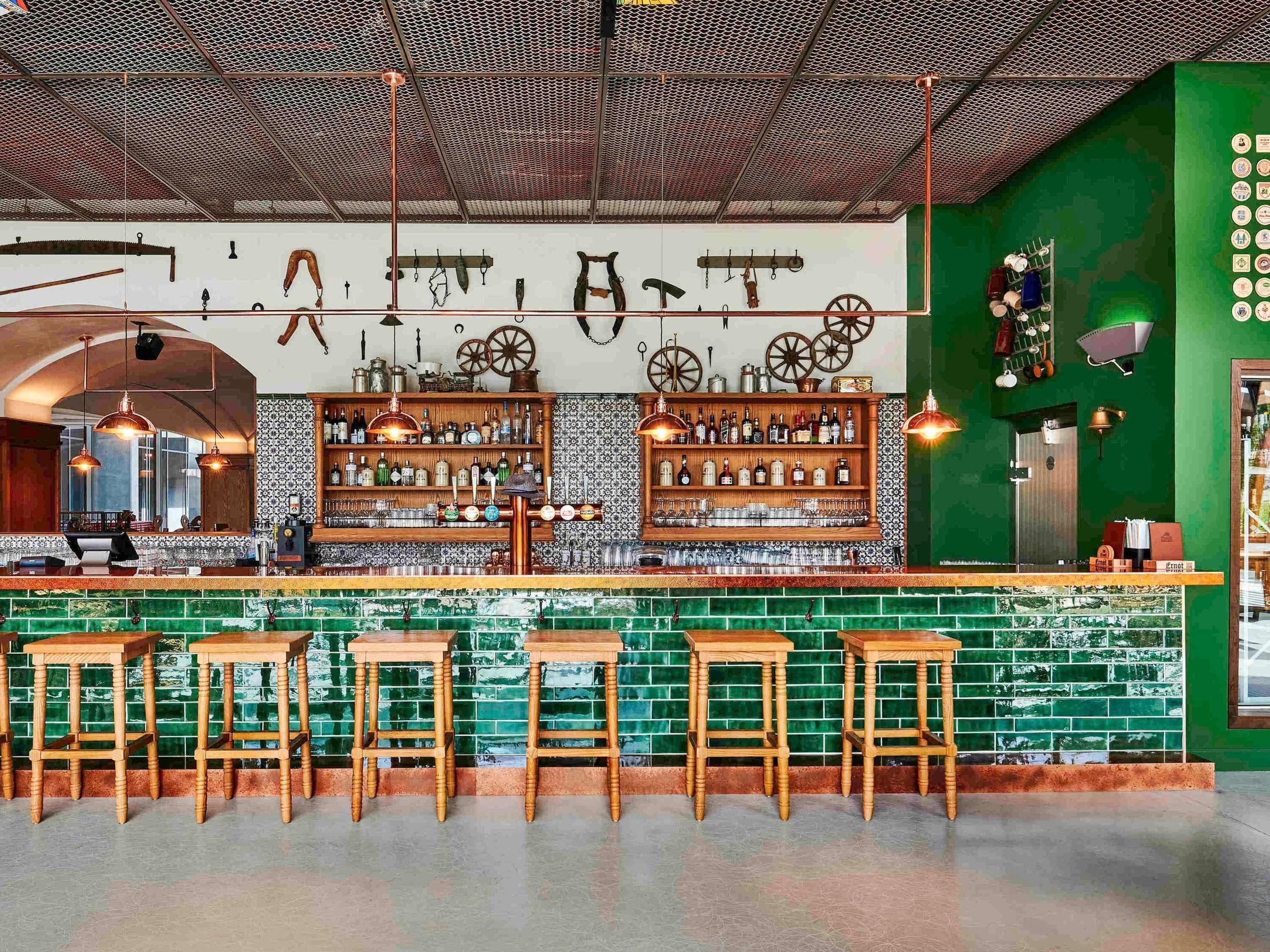 A bar area with wooden stools, a bar counter, and shelves of bottles.