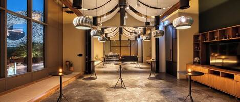Ein modernes Interieur mit einer zentralen Bar, mehreren Tischen mit Kerzen und Blick auf ein Gebäude.