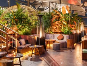 Un salón en la azotea con una escalera de madera, asientos acolchados y una variedad de plantas.