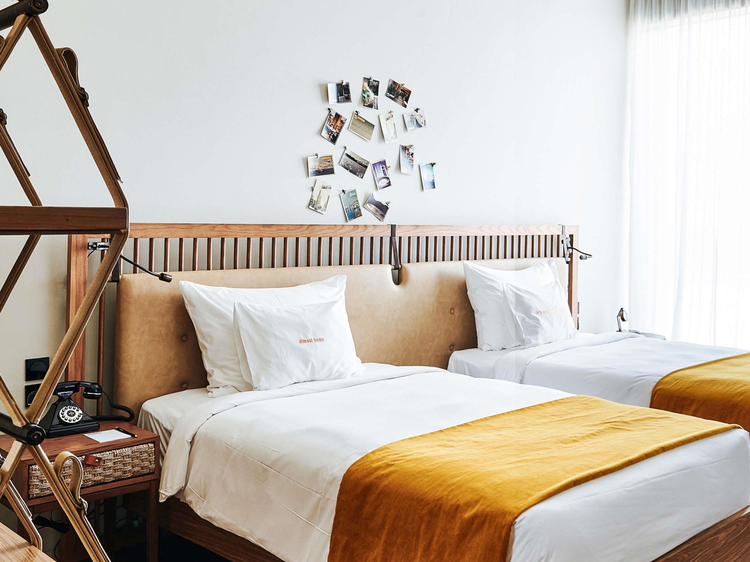 A hotel room with two beds, a wooden headboard, a wall-mounted telephone, and a wall of photos.