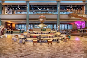 A spacious lobby with a central circular bookshelf, a staircase, and a bar area.